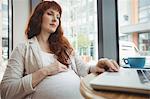 Pregnant businesswoman using laptop in office cafeteria
