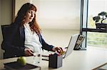 Pregnant businesswoman touching her belly while using laptop in office