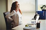Pregnant businesswoman holding her back while sitting on chair in office