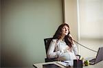 Pregnant businesswoman touching her belly while talking on telephone in office