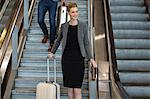 Businesswoman with luggage walking downstairs beside escalator at airport terminal