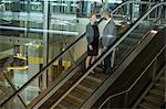 Businesspeople interacting with each other while going up on escalator at airport terminal