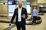 Businessman standing with luggage using mobile phone in waiting area at airport terminal