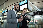 Business people holding boarding pass and using mobile phone in airport terminal
