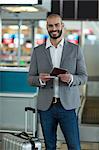 Portrait of smiling businessman with luggage checking his boarding pass at airport terminal