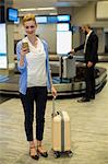 Businessman standing with luggage using mobile phone in waiting area at airport terminal