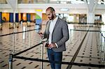 Businessman holding a boarding pass and checking his mobile phone at airport terminal