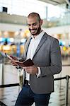 Smiling businessman holding a boarding pass and checking his mobile phone at airport terminal