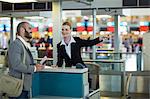 Airline check-in attendant showing direction to commuter at check-in counter in airport terminal