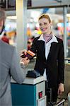 Airline check-in attendant handing passport to commuter at counter in airport terminal