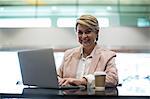 Portrait of smiling businesswoman using laptop in waiting area at airport terminal