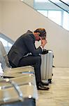 Tense businessman sitting in waiting area with luggage at airport terminal