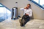 Businessman sitting on floor and using mobile phone in waiting area at airport terminal