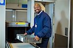 Portrait of smiling airport security officer holding a crate near conveyor belt at airport terminal