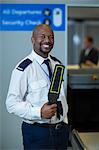 Portrait of smiling airport security officer holding metal detector in airport terminal