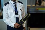 Mid section of airport security officer holding metal detector in airport terminal