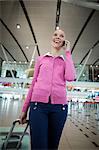 Female commuter with luggage talking on mobile phone in airport