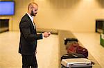 Businessman using mobile phone near baggage claim area at airport