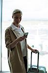 Businesswoman with luggage using mobile phone at airport