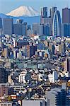 A telephoto view on a clear winter day captures a snow-capped Mt. Fuji rising dramatically beyond the skyscrapers, including Tokyo City Hall, in the Shinjuku District of Tokyo, Japan.