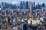 A telephoto view on a clear winter day captures a snow-capped Mt. Fuji rising dramatically beyond the skyscrapers (including Tokyo City Hall) of the Shinjuku District in Tokyo, Japan.