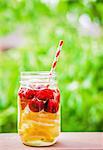 Fruity iced tea in a screw-top jar with a straw on a garden table