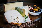 Various types of cheese on a chopping board and a dish of olives