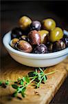 Green and black olives in a dish on a chopping board
