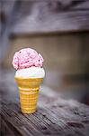 A scoop of coconut and a scoop of strawberry ice cream in an ice cream cone on a wooden table