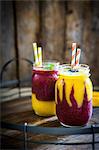 Colourful two layer mango and berry smoothies garnished with blackberries