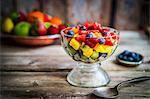 A colourful fruit salad in a jar on rustic wooden surface