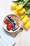 Muesli with yoghurt, blueberries and strawberries next to a bunch of yellow tulips