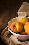 Peaches in a ceramic bowl on a wooden surface