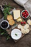 A cheese platter with sesame seed and wheat crackers, herbs, cherries and blackberries