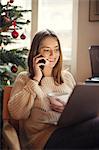 Woman using laptop and talking on cell phone in living room