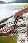 Person preparing sausages on barbecue grill
