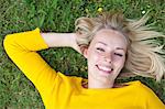 Portrait of a pretty blonde woman lying down in park smiling at camera