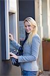 Pretty blonde woman using a cash machine and smiling at camera