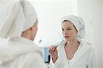 Woman in bathrobe brushing her teeth in front of the mirror