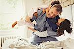 Multi-ethnic daughters playing and tackling father on bed