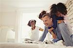 Multi-ethnic daughters tackling father on bed