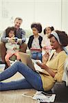 Multi-ethnic father and daughters playing behind mother working at laptop on living room floor