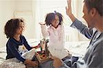 Father receiving Father's Day card from daughters and high-fiving on bed