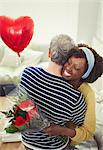 Wife receiving Valentine's Day rose bouquet and balloon, hugging husband