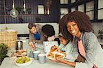 Portrait smiling mother eating breakfast toast with young family in kitchen