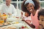 Portrait smiling mother eating breakfast with young family at table