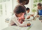 Mother watching daughter coloring in activity book in kitchen