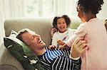 Playful multi-ethnic father and daughters tickling and laughing on sofa