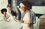 Mother reading newspaper and eating breakfast in kitchen with young family