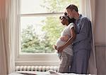 Affectionate pregnant couple in pajamas hugging at window